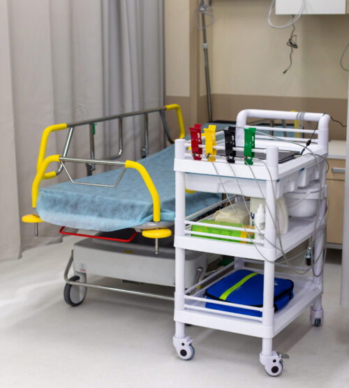 Modern hospital room equipped with a patient bed and a medical trolley with supplies Modern hospital room, in the emergency department, equipped with a bed for the patient and a medical trolley with supplies